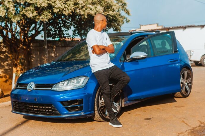 Bilägare lutar sig mot en blå Volkswagen på en solig uppfart